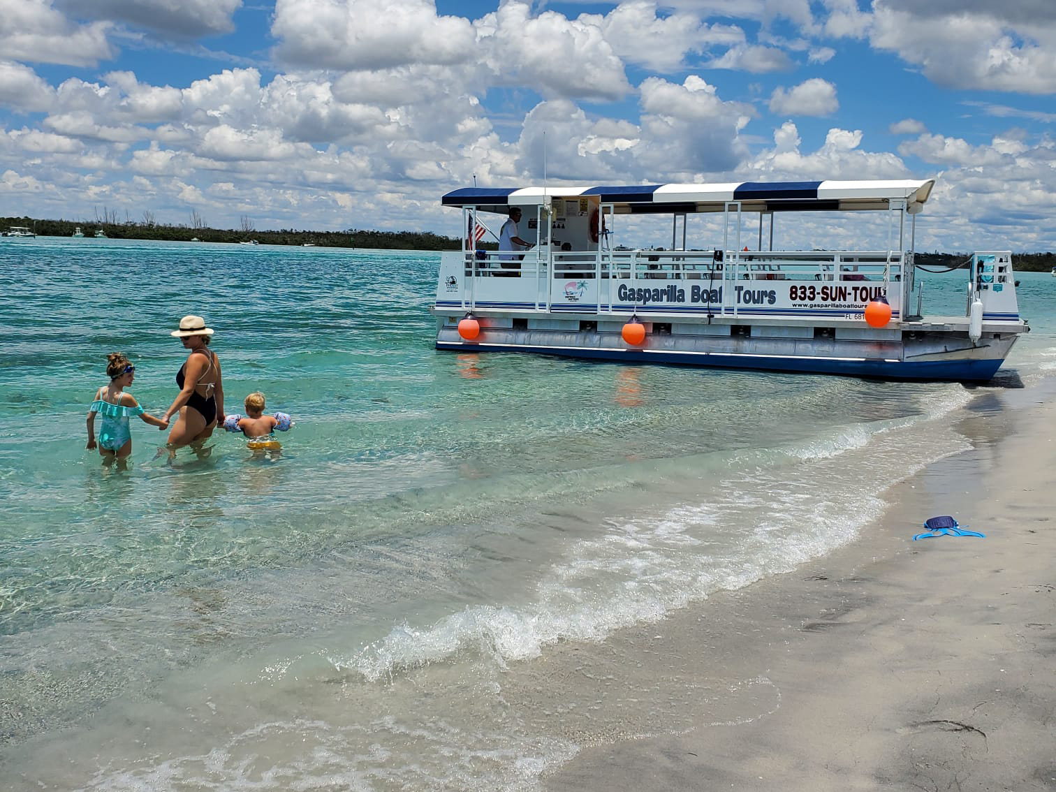 three people in the water at the beach by a gasparilla boat tours boat